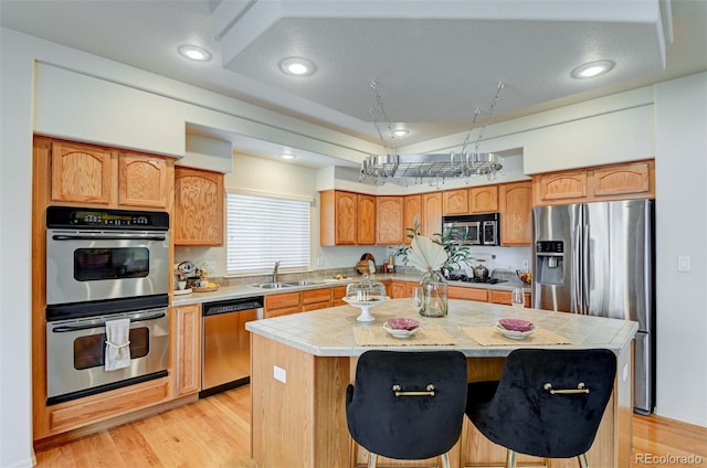 kitchen with sink, light wood-type flooring, appliances with stainless steel finishes, a kitchen island, and a breakfast bar area