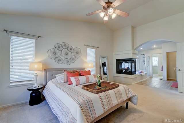 bedroom with light carpet, a multi sided fireplace, ceiling fan, and lofted ceiling