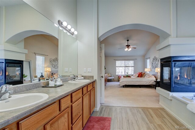 bathroom featuring vanity, vaulted ceiling, ceiling fan, wood-type flooring, and a multi sided fireplace