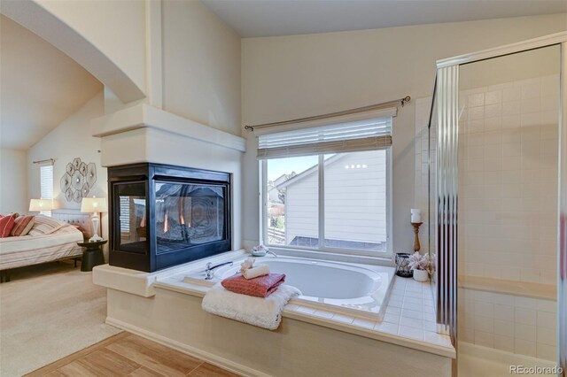 bathroom with a bathing tub, a multi sided fireplace, and vaulted ceiling