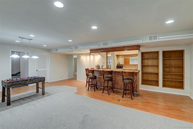 bar featuring decorative light fixtures, light hardwood / wood-style flooring, and built in features