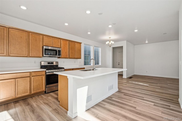 kitchen with sink, an inviting chandelier, light wood-type flooring, appliances with stainless steel finishes, and an island with sink