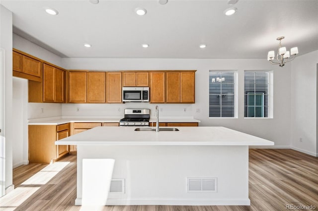 kitchen featuring sink, decorative light fixtures, stainless steel appliances, and a center island with sink