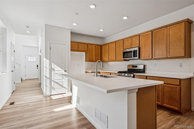 kitchen featuring stainless steel appliances, a kitchen island with sink, sink, and light wood-type flooring