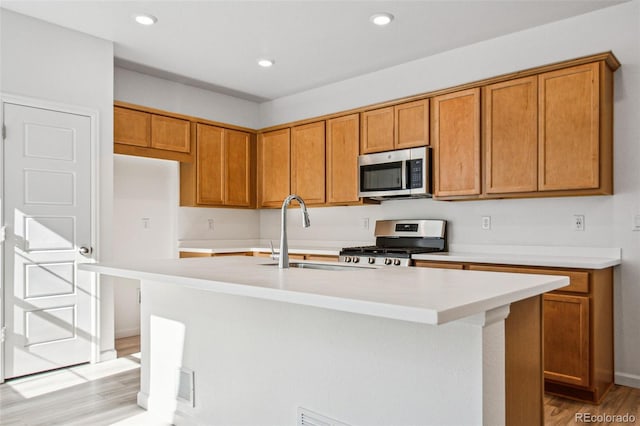 kitchen featuring appliances with stainless steel finishes, sink, an island with sink, and light wood-type flooring