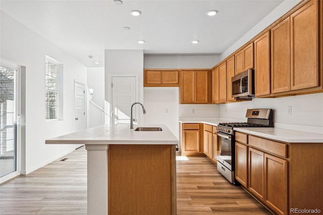 kitchen with sink, light wood-type flooring, an island with sink, and appliances with stainless steel finishes