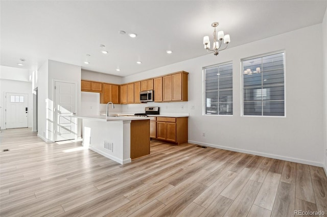 kitchen featuring appliances with stainless steel finishes, sink, light hardwood / wood-style floors, and a kitchen island with sink