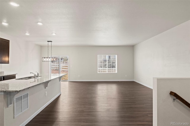 unfurnished living room featuring dark wood-style floors, visible vents, a sink, and baseboards