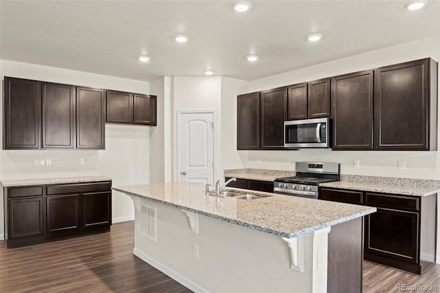 kitchen featuring dark wood-style floors, appliances with stainless steel finishes, a breakfast bar area, and a sink