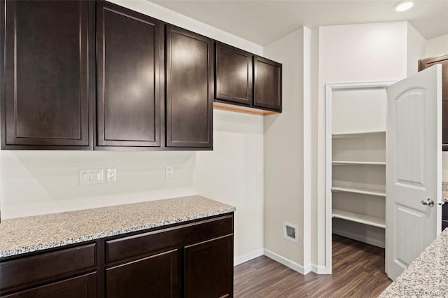 kitchen with dark wood-type flooring, baseboards, light stone counters, and dark brown cabinets