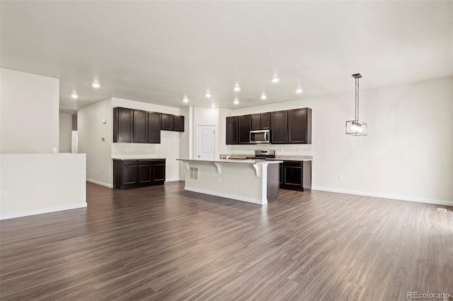 kitchen featuring recessed lighting, open floor plan, appliances with stainless steel finishes, dark wood-style floors, and a kitchen bar