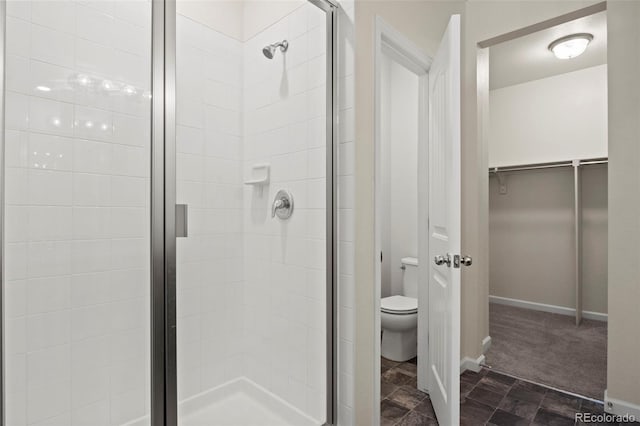 bathroom with toilet, a shower stall, baseboards, and a walk in closet