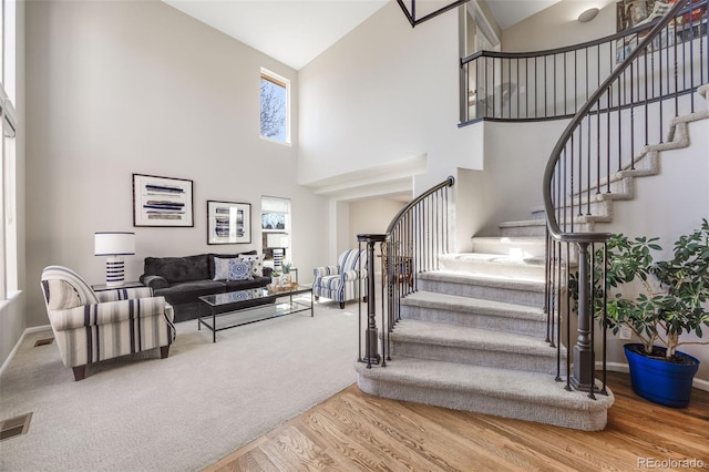 stairway with visible vents, a towering ceiling, baseboards, and wood finished floors