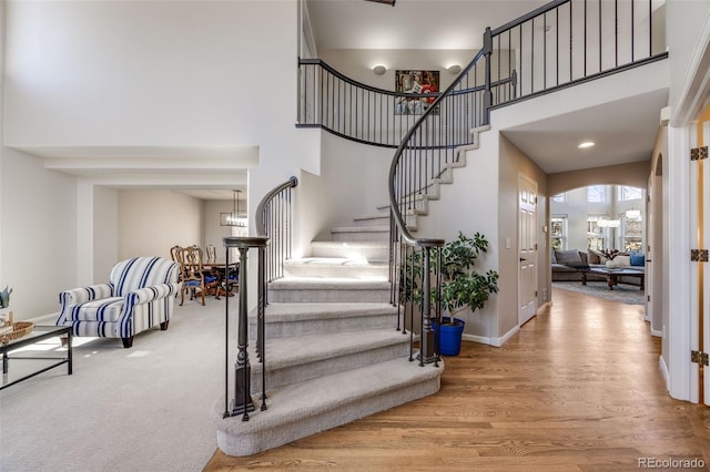 entrance foyer featuring arched walkways, stairway, a towering ceiling, wood finished floors, and baseboards