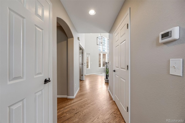 hall featuring light wood-style floors, arched walkways, and baseboards