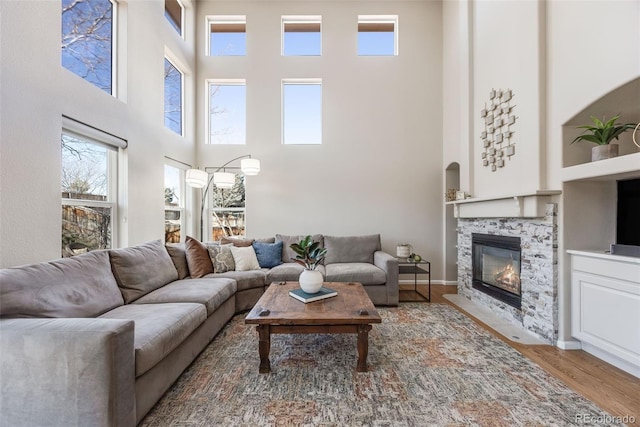 living room featuring a fireplace with flush hearth, a high ceiling, baseboards, and wood finished floors