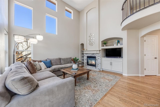 living area featuring arched walkways, built in shelves, baseboards, light wood-style floors, and a glass covered fireplace