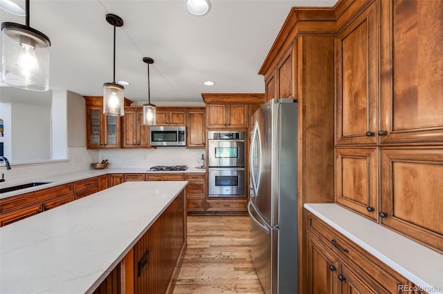 kitchen featuring appliances with stainless steel finishes, brown cabinetry, a sink, and decorative light fixtures