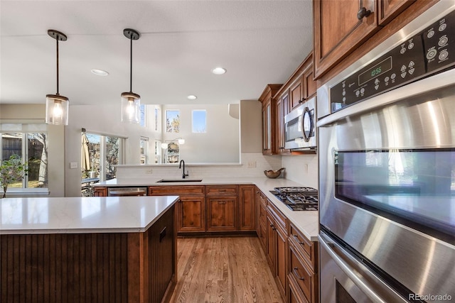 kitchen with brown cabinetry, hanging light fixtures, stainless steel appliances, light countertops, and a sink