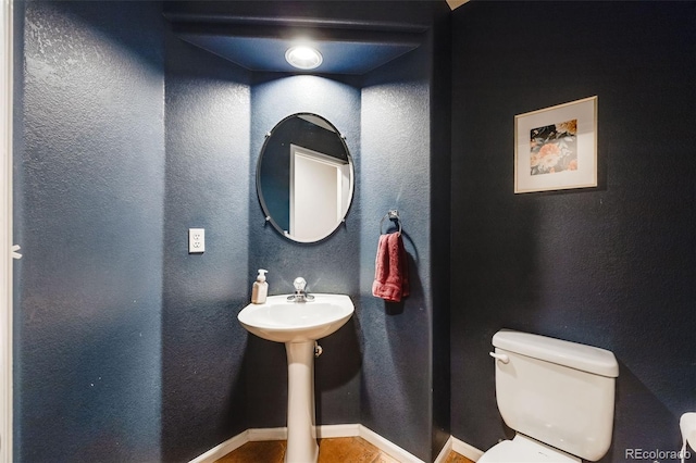 bathroom featuring a textured wall, toilet, and baseboards