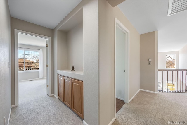 corridor with light carpet, visible vents, and baseboards