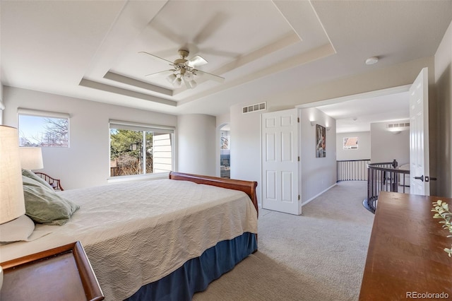 carpeted bedroom featuring a ceiling fan, a tray ceiling, visible vents, and baseboards