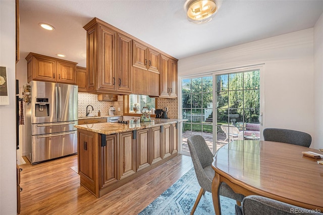 6248 W 75th, Arvada, CO 80003 - kitchen featuring stainless steel fridge, brown cabinetry, light wood-type flooring, a peninsula, and light stone counters