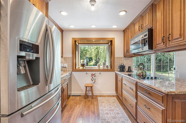 6248 W 75th, Arvada, CO 80003 - kitchen featuring stainless steel appliances, brown cabinets, light stone counters, light wood-type flooring, and backsplash