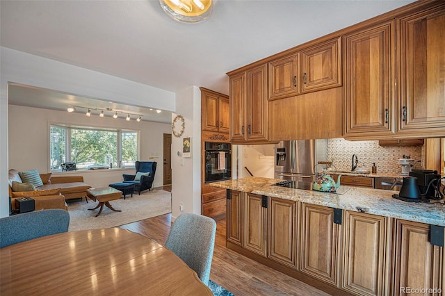 6248 W 75th, Arvada, CO 80003 - kitchen featuring black appliances, light wood-style floors, brown cabinets, open floor plan, and light stone countertops