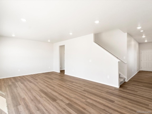 unfurnished living room with recessed lighting, baseboards, wood finished floors, and stairs