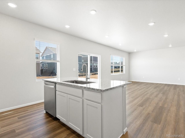 kitchen featuring a sink, light stone countertops, a center island with sink, wood finished floors, and stainless steel dishwasher