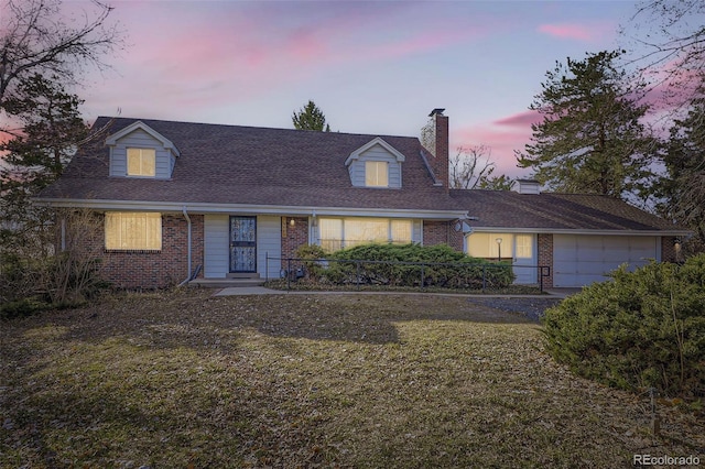 cape cod house with a yard, an attached garage, brick siding, and a chimney