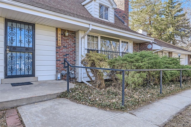 doorway to property featuring brick siding, roof with shingles, and a chimney