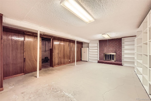 finished basement with wooden walls, a brick fireplace, and a textured ceiling