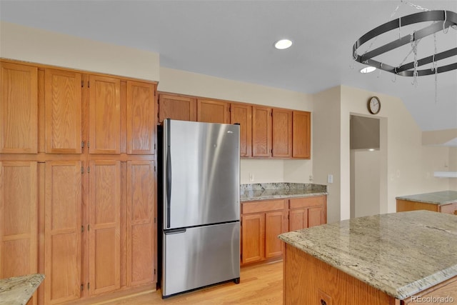 kitchen with light stone countertops, a kitchen island, light wood-type flooring, and stainless steel refrigerator