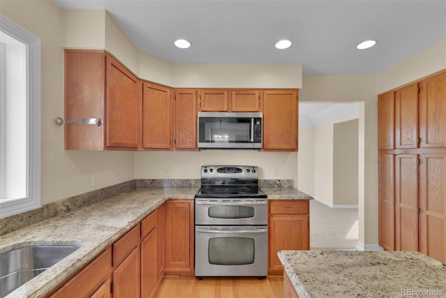 kitchen featuring stainless steel appliances, sink, light stone counters, and light hardwood / wood-style flooring