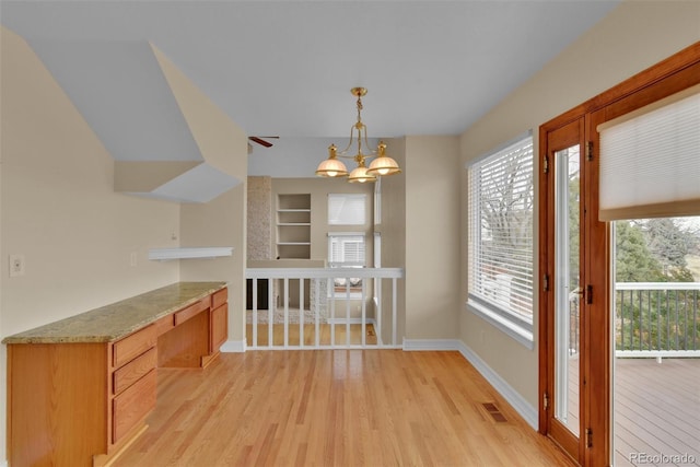 unfurnished dining area with built in features, built in desk, a notable chandelier, and light wood-type flooring