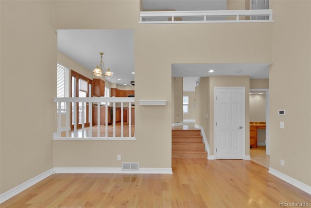 empty room with a notable chandelier, a towering ceiling, a healthy amount of sunlight, and light wood-type flooring