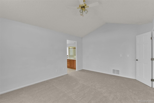 spare room with ceiling fan, light colored carpet, vaulted ceiling, and a textured ceiling