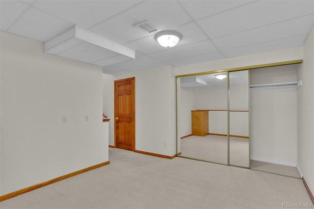 unfurnished bedroom with light colored carpet, a paneled ceiling, and a closet