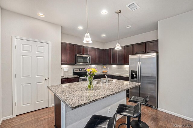 kitchen featuring stainless steel appliances, wood finished floors, a sink, tasteful backsplash, and light stone countertops