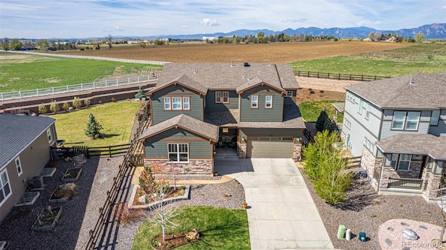 craftsman inspired home featuring concrete driveway, a rural view, fence, and stone siding