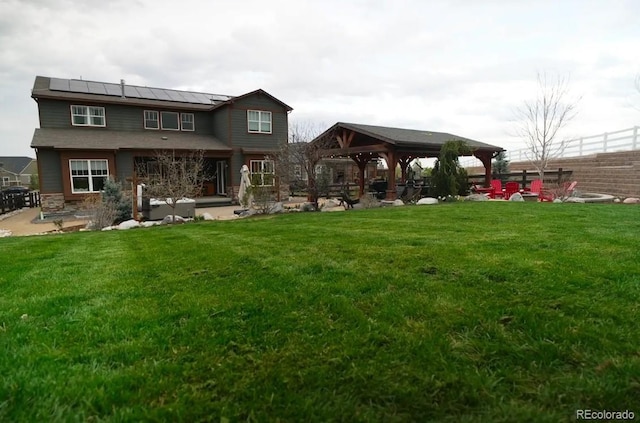 rear view of house with a lawn, a gazebo, a standing seam roof, and solar panels
