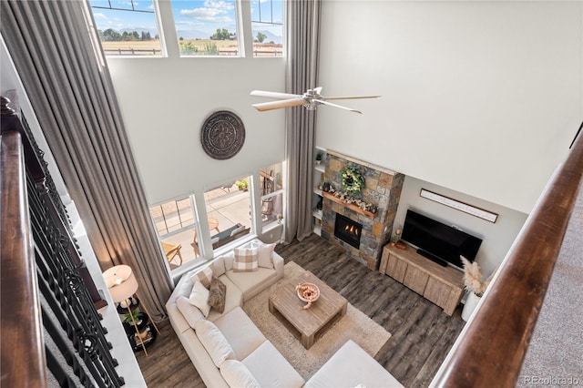 living area featuring a towering ceiling, wood finished floors, a fireplace, and ceiling fan