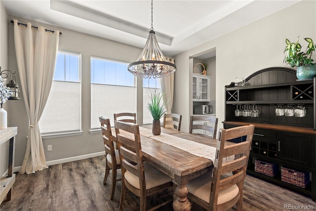 dining room featuring an inviting chandelier, a raised ceiling, baseboards, and dark wood-style floors