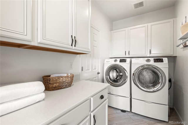 clothes washing area featuring visible vents, washer and clothes dryer, and cabinet space