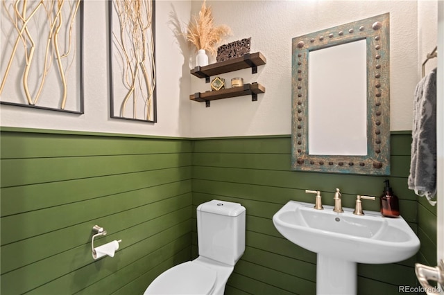 half bathroom with toilet, wainscoting, and a sink