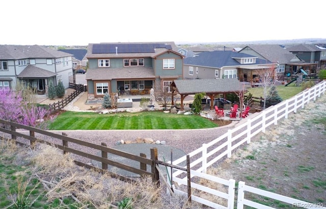 back of property featuring a residential view, a patio area, a fenced backyard, roof mounted solar panels, and a yard