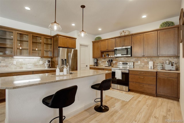 kitchen featuring pendant lighting, light hardwood / wood-style flooring, a kitchen island with sink, stainless steel appliances, and sink