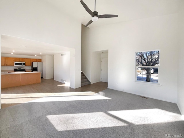 unfurnished living room featuring ceiling fan, light colored carpet, and a high ceiling